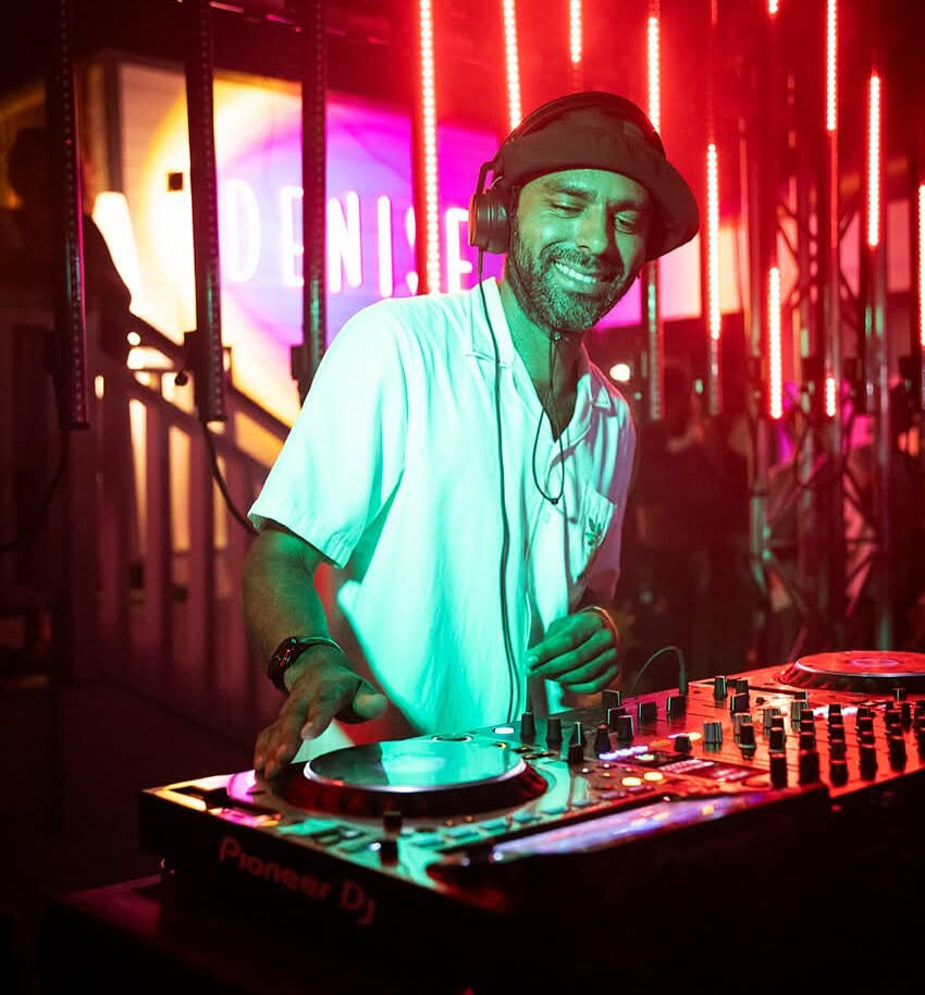 Saint Paul playing a DJ set behind Pioneer CDJs under red club lighting